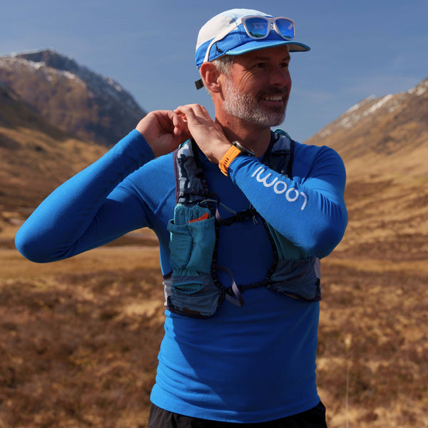 Man adjusting running backpack wearing Loomi Base Layer with Scottish mountain in the background.